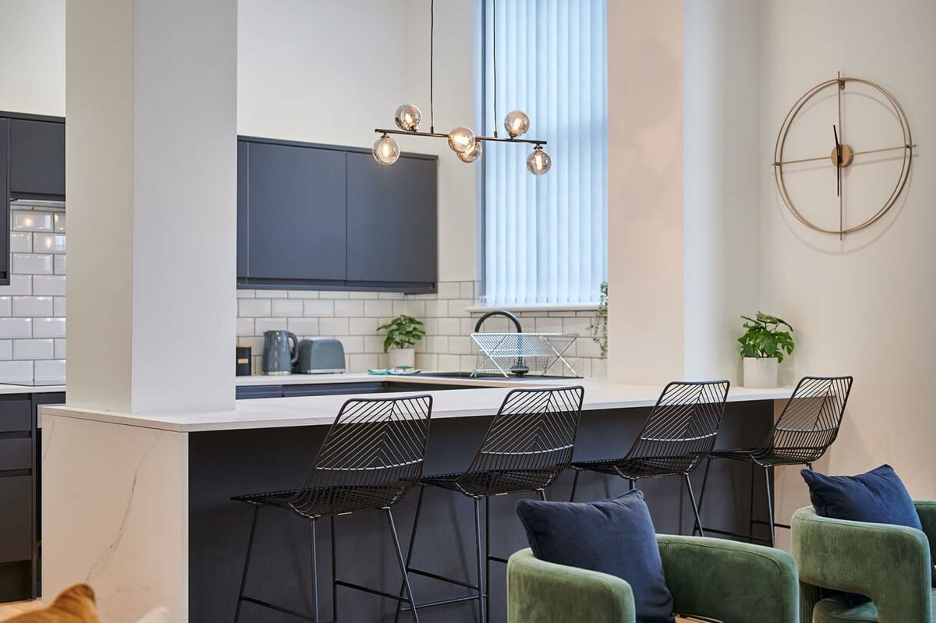 A modern kitchen with a central island, black wire chairs, and a round wall decoration.