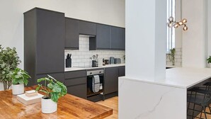A modern kitchen with dark cabinets, a white countertop, and a wooden dining table. - Host Stay Princes Place Hideaway III (Liverpool)