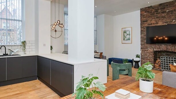 A modern kitchen with dark cabinets, a wooden dining table with potted plants, and a brick fireplace. - Host Stay Princes Place Hideaway III (Liverpool)