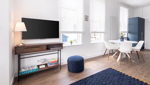 A modern living room with a flat-screen TV, a coffee table, a blue ottoman, and a dining area with white chairs and a blue cabinet. - Host Stay Sanderling Chase (Scarborough)
