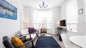 A modern living room with a sofa, chairs, a coffee table, a TV, and a large window with blinds. - Host Stay Sanderling Chase (Scarborough)