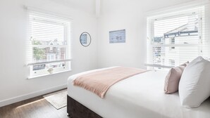 A bedroom with a bed, two windows, a wall clock, and a small painting. - Host Stay Sanderling Chase (Scarborough)