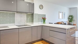 Uma cozinha moderna com armários cinzas, piso de madeira em padrão herringbone e um relógio na parede.