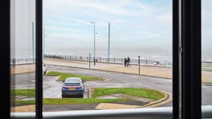 Uma estrada costeira com um carro azul estacionado, uma faixa de pedestres e vista para o mar.