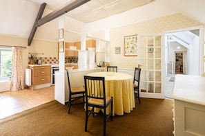 A dining area with a round table and chairs, a kitchen in the background, and a view through a glass door. - Host Stay Upper Lodge (Alnwick)