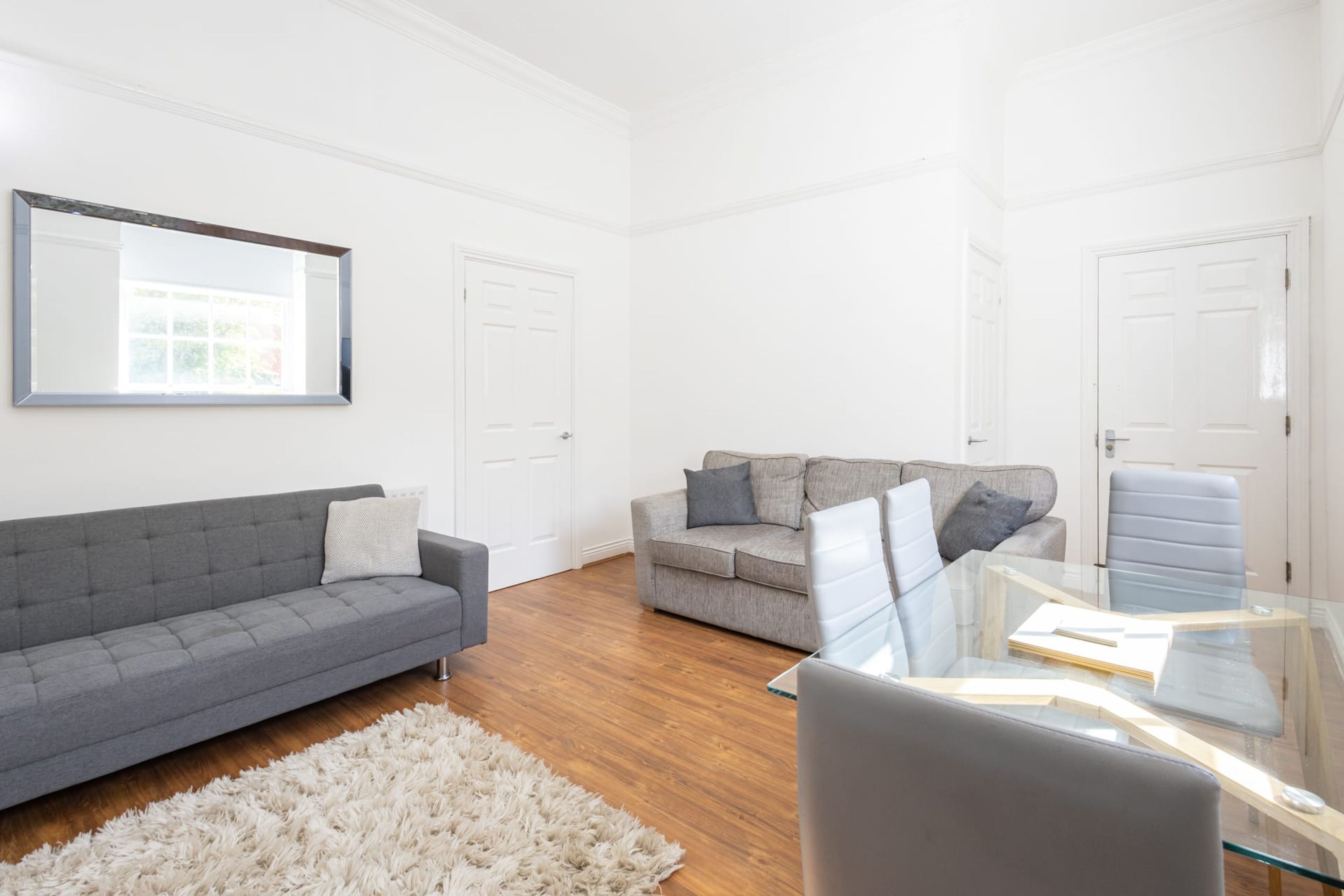 A modern living room with a grey sofa, a grey couch, and a glass coffee table.