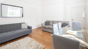 Een moderne woonkamer met een grijze bank, een grijze slaapbank en een glazen salontafel.