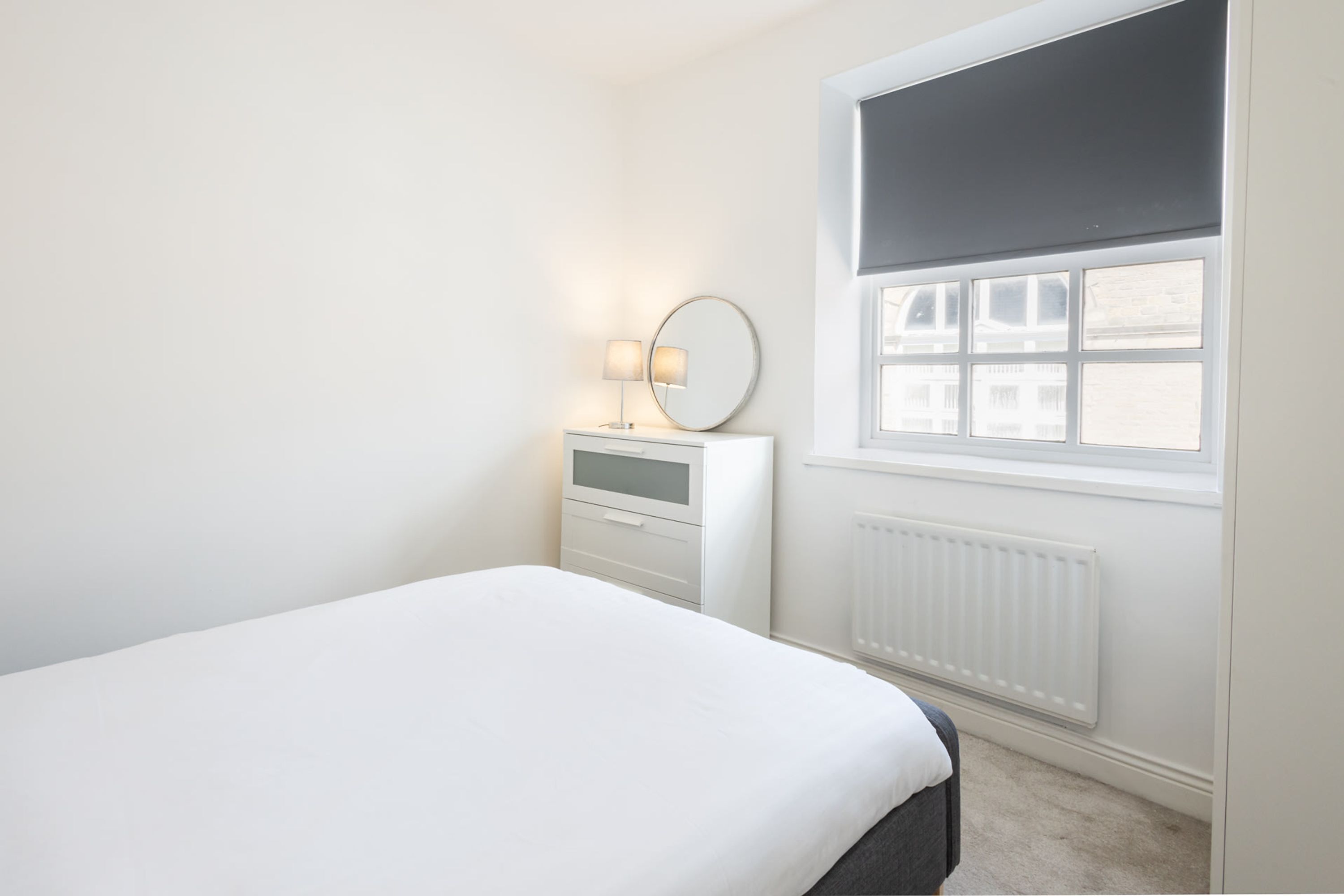 Une chambre à coucher avec un lit, une commode avec un miroir et une fenêtre avec des stores.