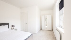 Een slaapkamer met een bed, nachtkastje, garderobe en een raam.