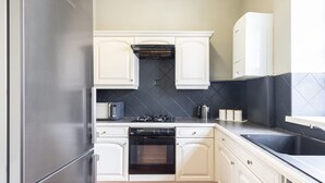 Een moderne keuken met witte kasten, een roestvrijstalen koelkast, een inbouwoven, een gasfornuis en een spoelbak met zwart aanrecht.