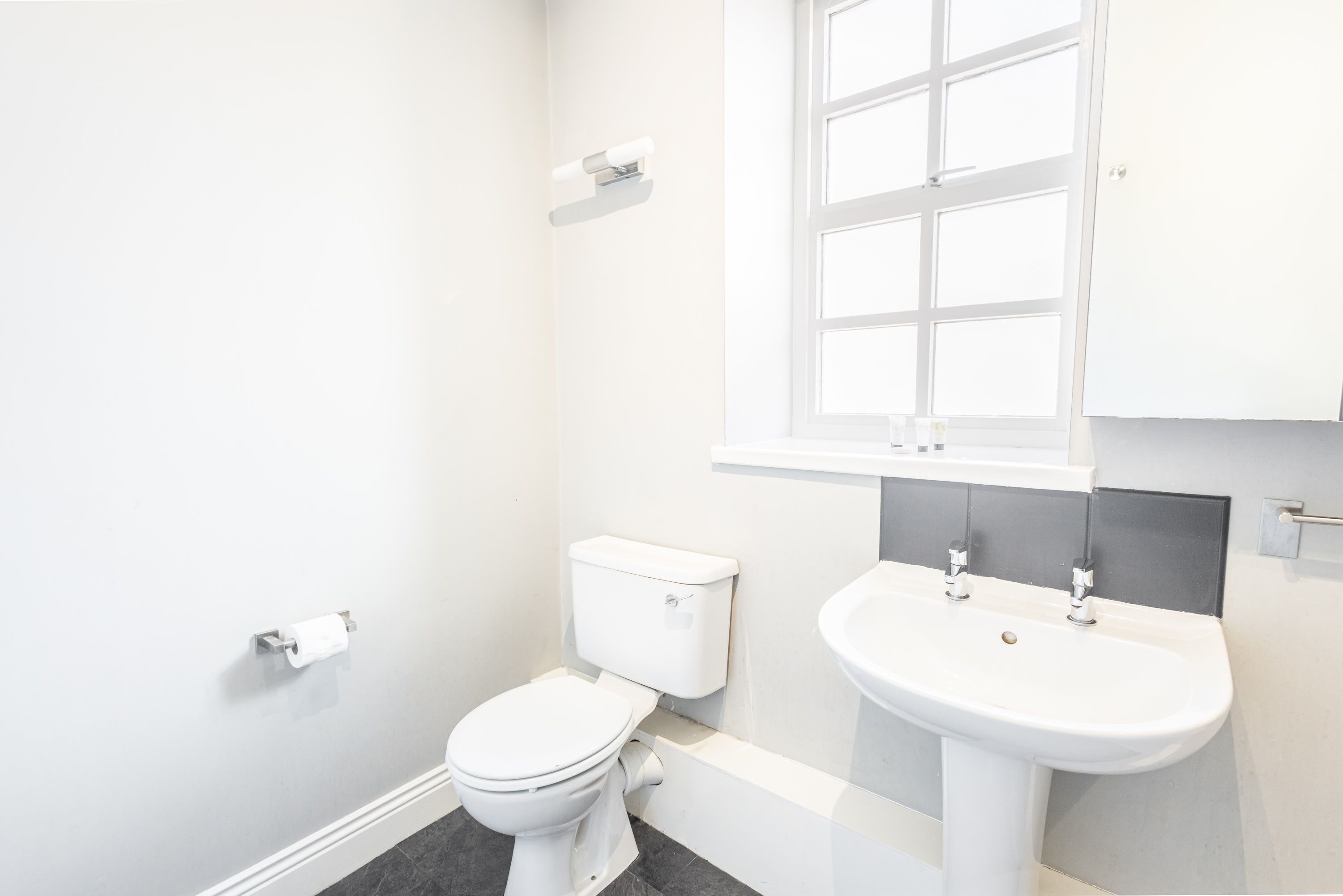 A small, white bathroom with a toilet, sink, and window.