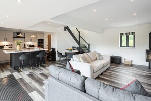 A modern kitchen with a central island, bar stools, and a dining area with a sofa and chairs. - Host Stay The Stable (Ashbourne)