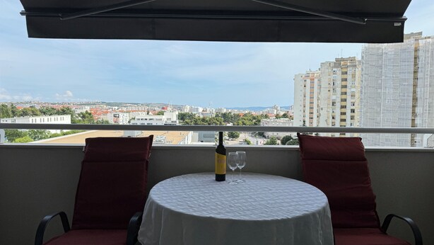 A balcony with a table, two chairs, and a bottle of wine. - Spacious 2-bedroom apartment in fabulous Zadar with WiFi, AC, free parking (Zadar)