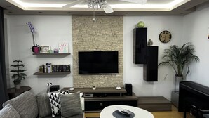 A modern living room with a flat-screen TV mounted on a brick wall, a fireplace, a clock, and a potted plant. - Spacious 2-bedroom apartment in fabulous Zadar with WiFi, AC, free parking (Zadar)
