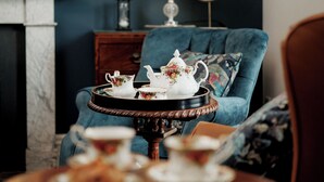 A cozy living room with a blue armchair, a round table with a teapot and cups, and a framed picture on the wall.