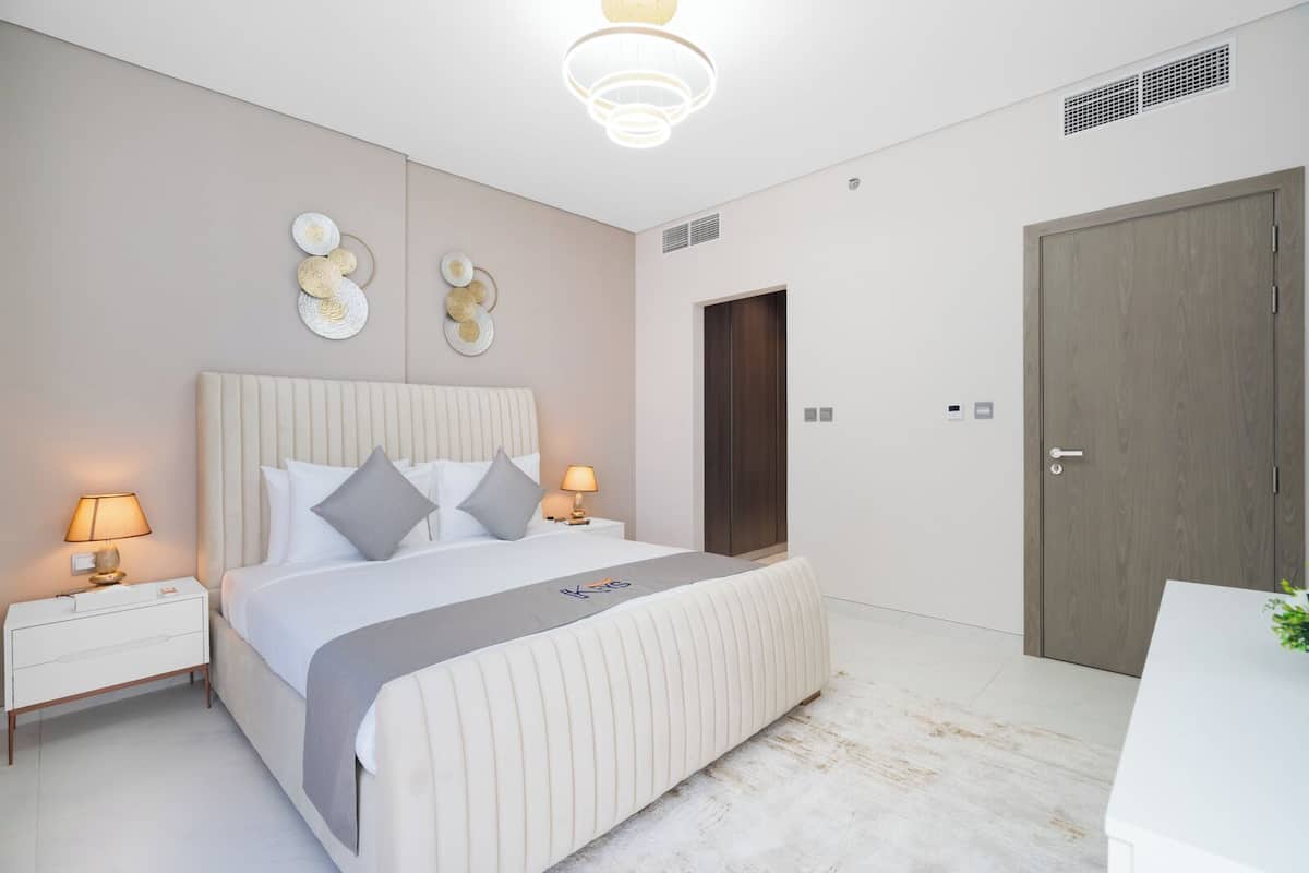 A modern bedroom with a large bed, bedside tables with lamps, a wardrobe, and decorative wall art.