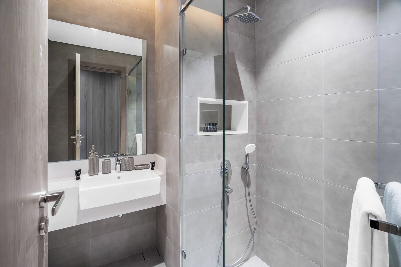 A modern bathroom with a glass shower enclosure, a white sink with a mirror above, and a towel rack.