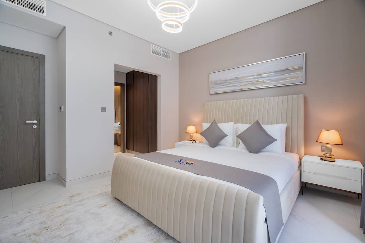 A modern hotel room with a large bed, two bedside tables, a ceiling light, and a painting on the wall.