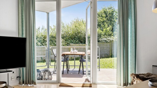A modern living room with a large sliding glass door leading to an outdoor patio. - Gudhjem Søpark Lejl. 57 (Gudhjem)