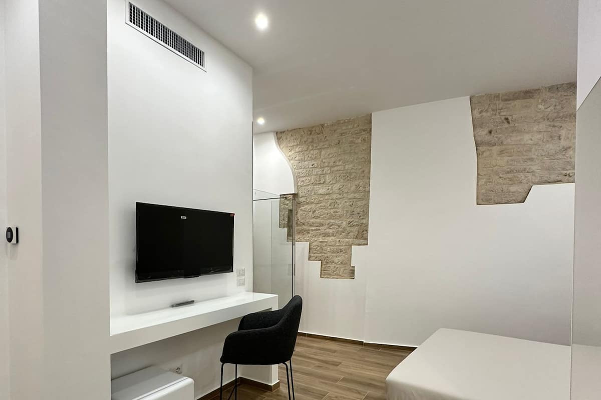 A modern bedroom with a bed, a desk with a TV, a chair, and a wardrobe.