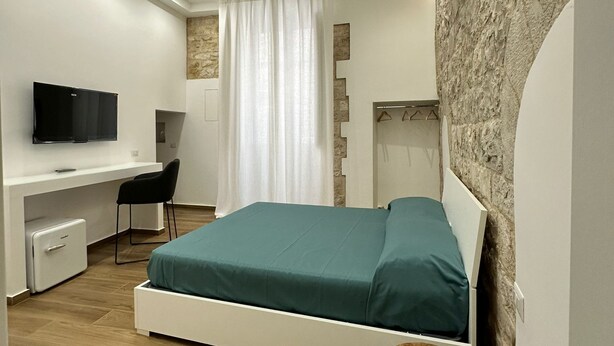 A modern bedroom with a bed, a desk, a chair, a television, and a stone accent wall. - Le Stanze Ritrovate (Trani)