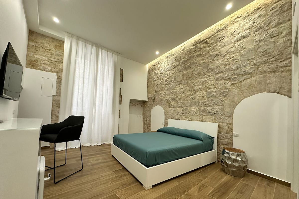 A modern bedroom with a stone accent wall, a bed, a desk, and a chair.