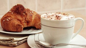A croissant and a cup of coffee on a table with a spoon. - Le Stanze Ritrovate (Trani)
