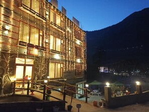 A hotel with a rustic exterior, a wooden deck, and a mountain backdrop. - 17 Milestone Riverside by Shivaneel Hospitality (Manali)