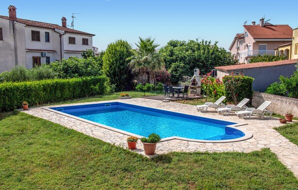 A rectangular swimming pool with a stone border, surrounded by a grassy lawn and potted plants.