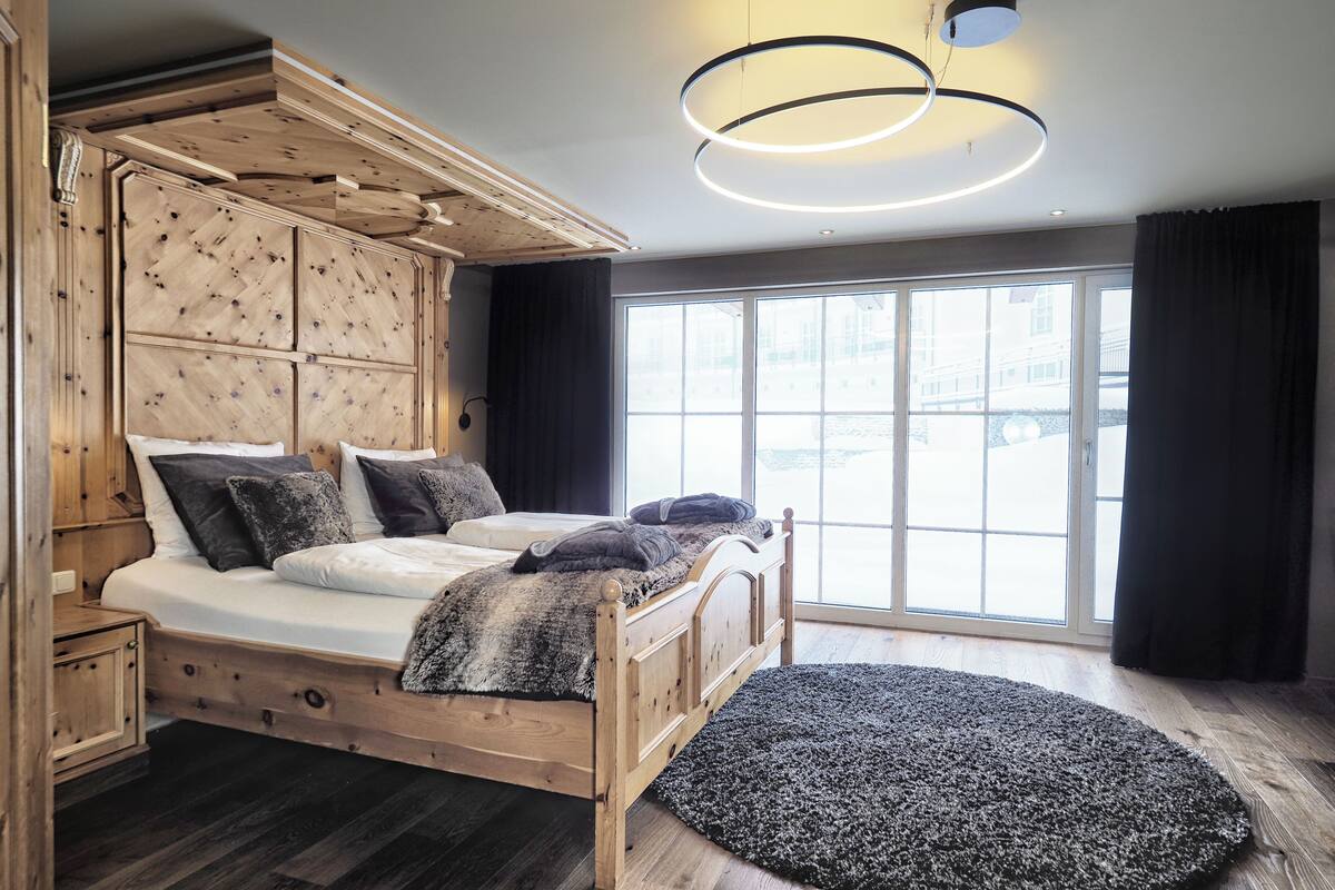 Un lit en bois avec une tête de lit, une grande fenêtre et un luminaire de forme circulaire.