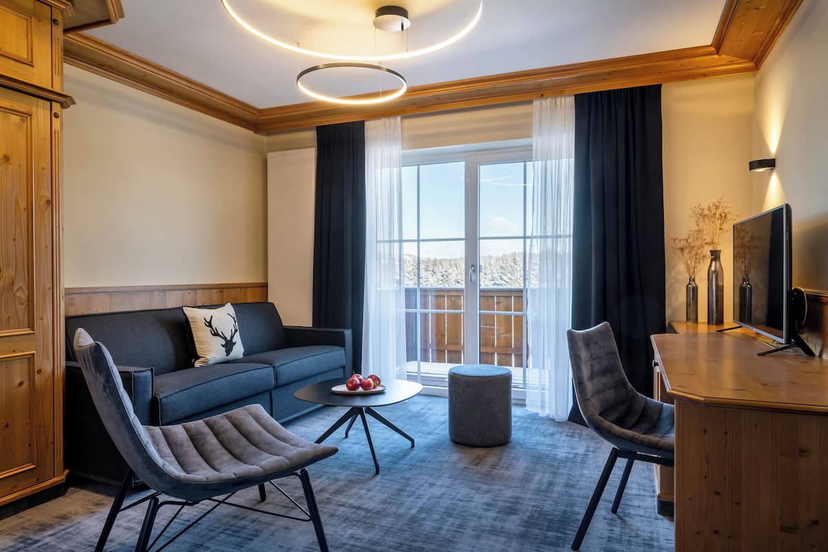 Un salon moderne comprenant un canapé, deux fauteuils, une table basse ronde et un bureau en bois avec un téléviseur.