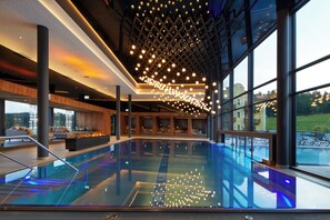 A modern indoor swimming pool with a glass floor, surrounded by seating areas and large windows offering views of the outside. - Wellness & Naturresort Reischlhof (Wegscheid)