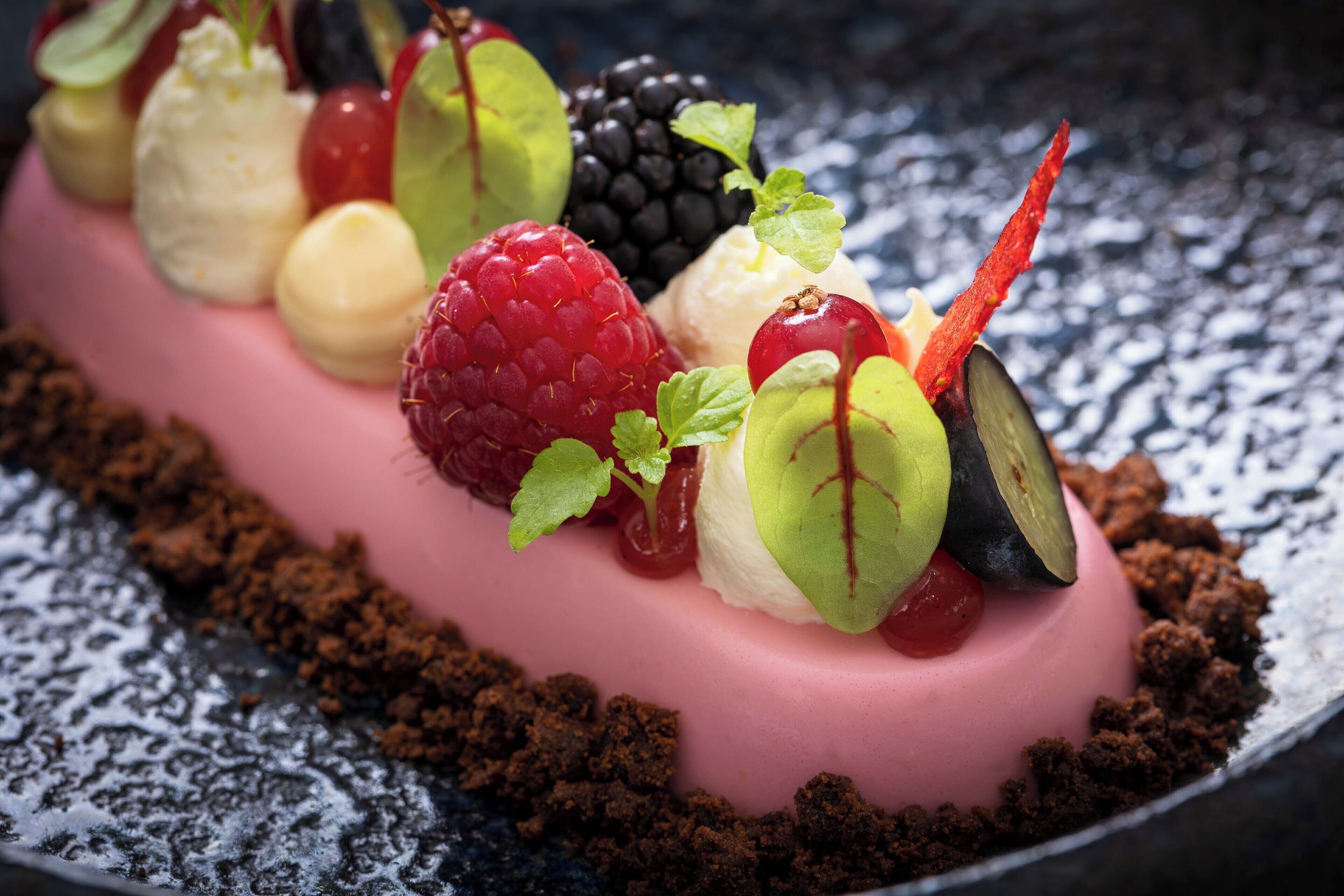 A dessert with various fruits and a pink base, placed on a textured surface.
