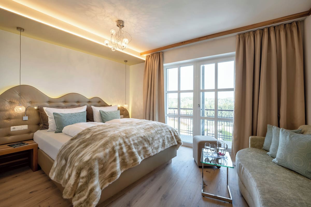 Une chambre moderne avec un grand lit, un canapé, une table basse en verre et une vue sur l’extérieur.