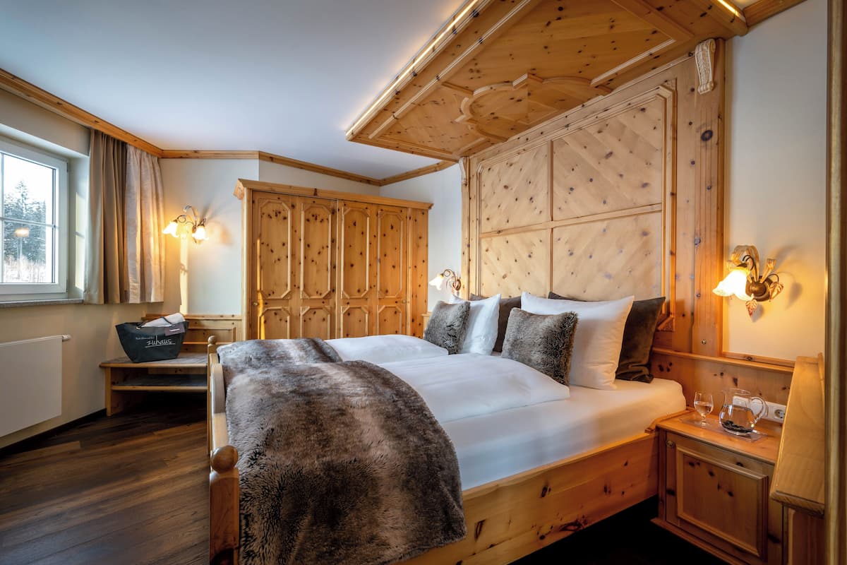 Un lit en bois avec un plaid en fourrure, une table de chevet avec un verre d’eau et une armoire en bois.