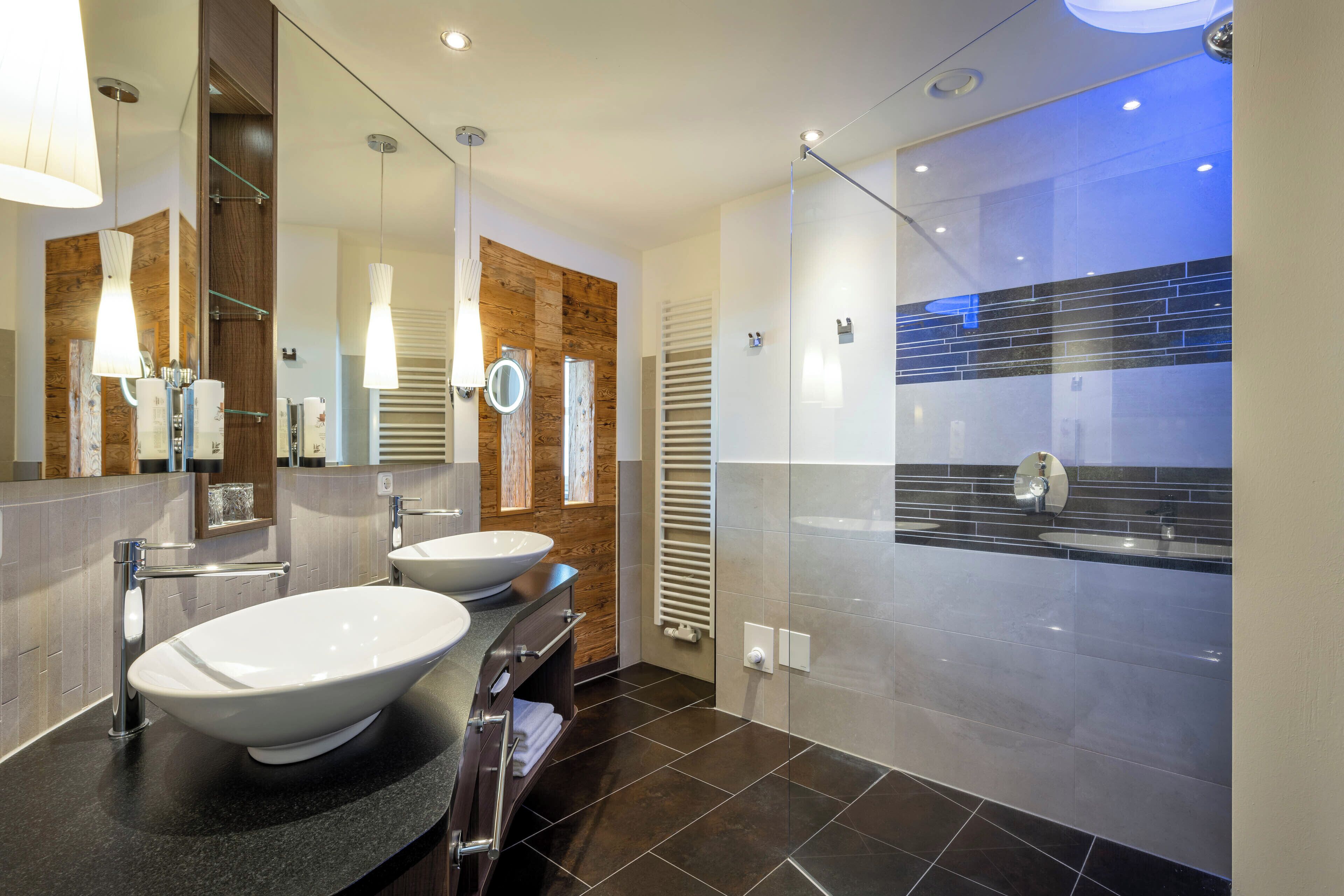 A modern bathroom with two sinks, a large mirror, and a walk-in shower.