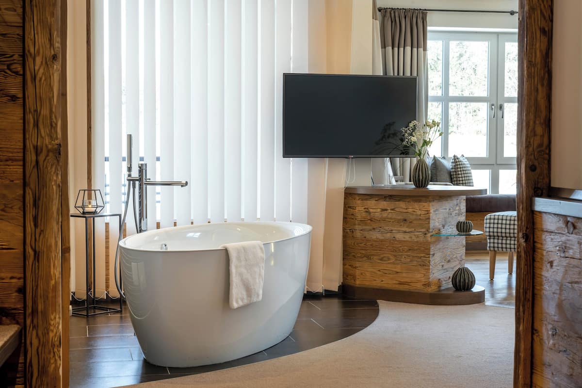 Une salle de bain moderne avec une baignoire sur pieds, un téléviseur fixé au mur et un meuble-lavabo en bois.