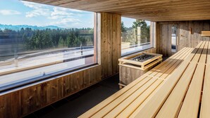 Un interior de madera con ventanas amplias, una sauna y vistas a un área boscosa.