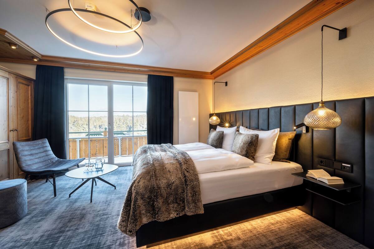 Une chambre d’hôtel moderne avec un grand lit, une table basse ronde, un fauteuil et une vue sur l’extérieur.