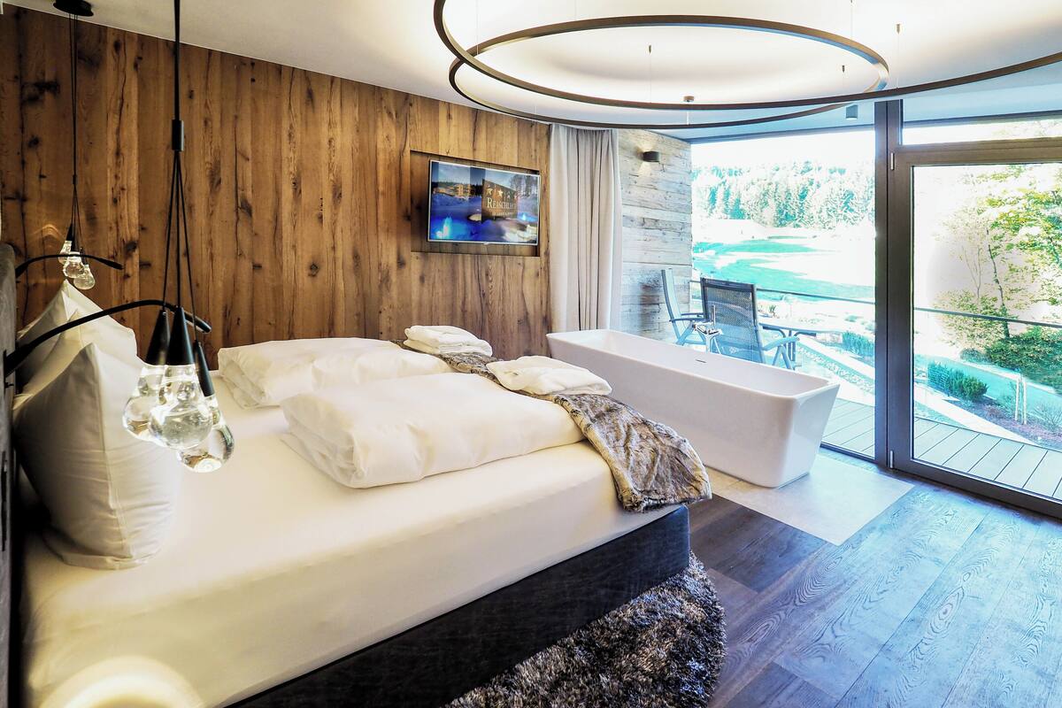 Une chambre moderne avec un grand lit, une baignoire et une vue sur un jardin, accessible par une porte-fenêtre coulissante.