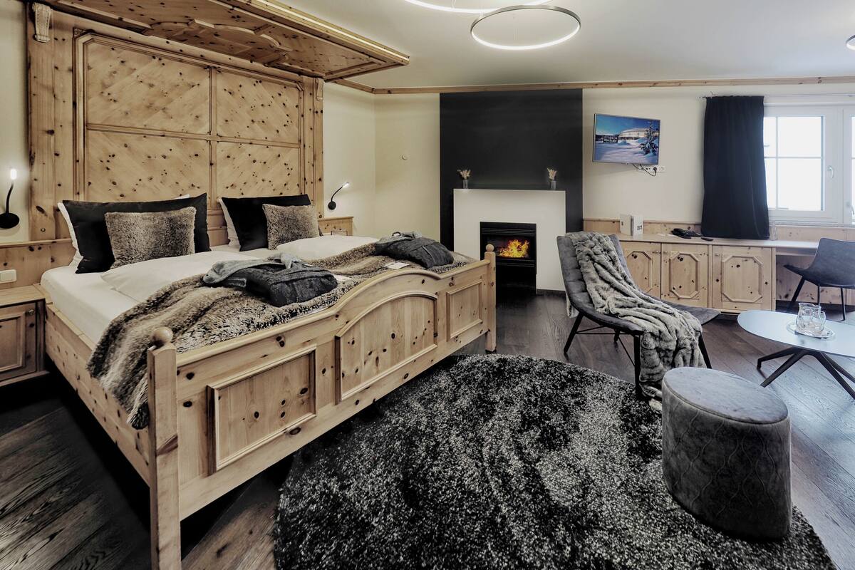 Une chambre confortable avec un lit en bois, une cheminée, un fauteuil confortable et un coin repas.