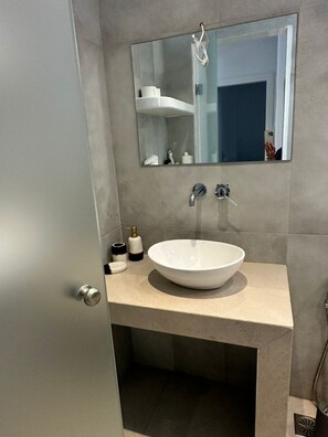 A modern bathroom with a large white sink, a mirror above it, and a door to the left. - ENE'S Mykonos (Mykonos)
