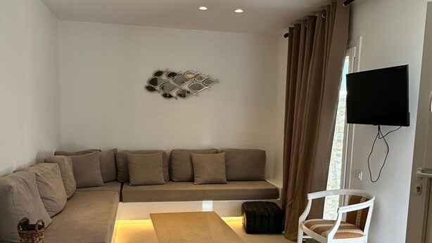 A modern living room with a sectional sofa, a wooden coffee table, and a white armchair. A flat-screen TV is mounted on the wall. - ENE'S Mykonos (Mykonos)