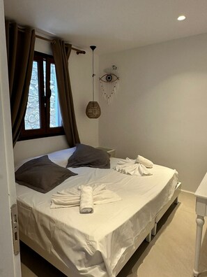A neatly made bed with white linens, a bedside table, and a window with curtains. - ENE'S Mykonos (Mykonos)