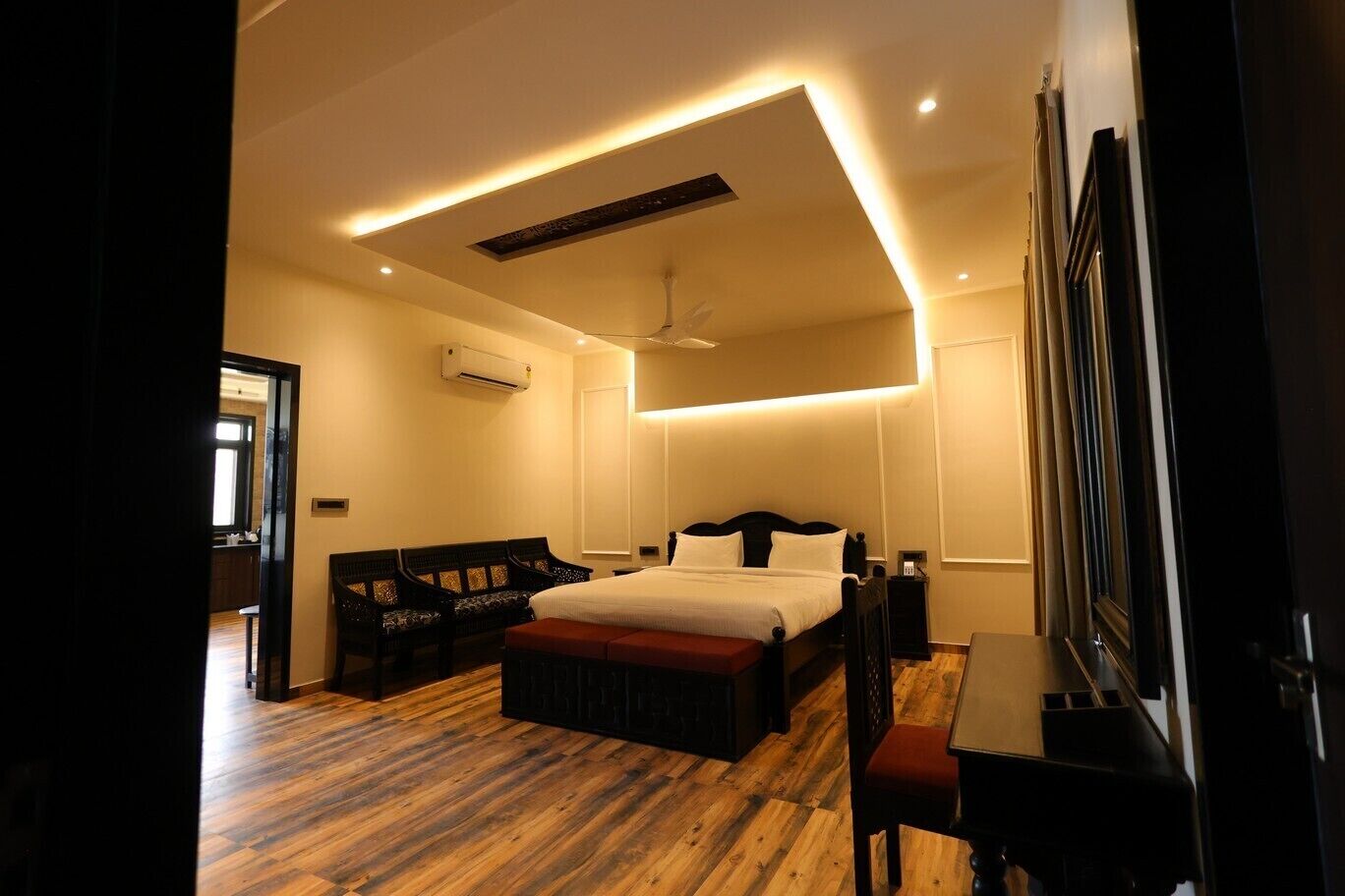 Une chambre à coucher moderne avec un plancher en bois, un lit avec une literie blanche, un banc, un bureau et un ventilateur de plafond.