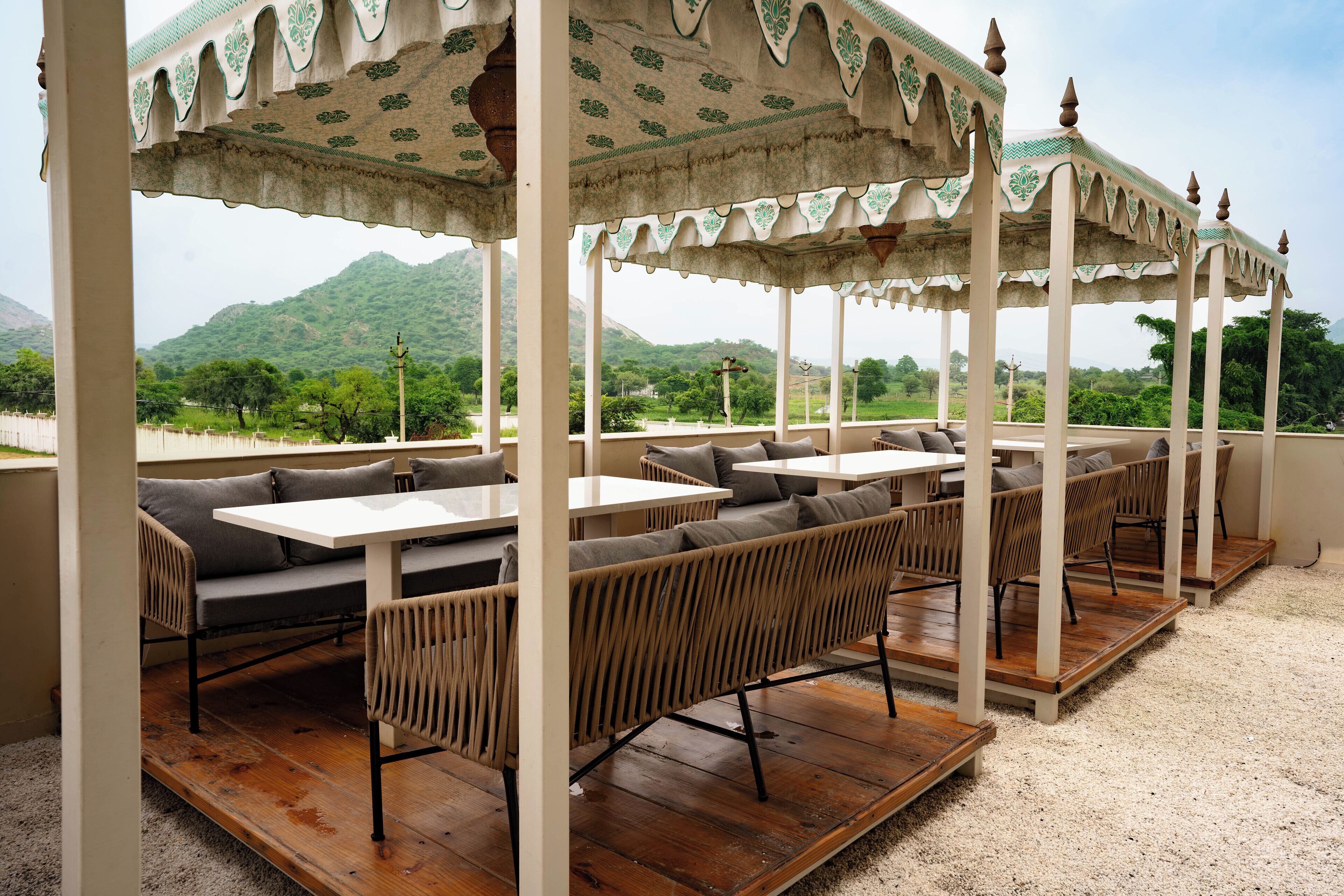 A covered outdoor seating area with tables and sofas, overlooking a mountainous landscape.