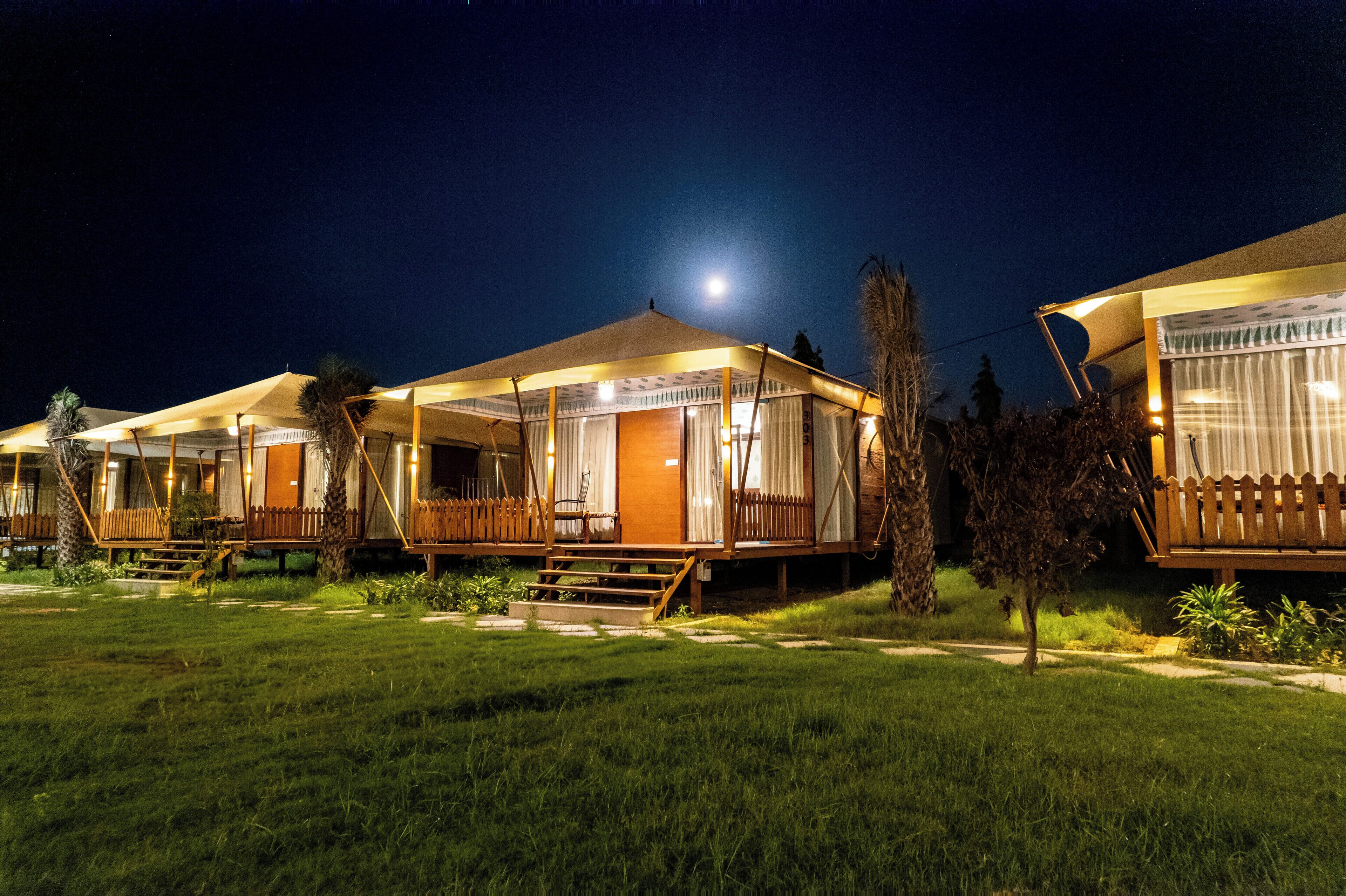 A row of cabins with wooden decks and covered porches, connected by a pathway, under a night sky with a visible moon.