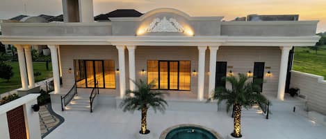 A large, modern house with a swimming pool, palm trees, and a well-lit entrance.