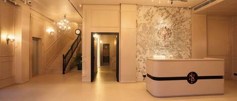 A spacious lobby with a grand staircase, a reception desk, and elegant chandeliers.