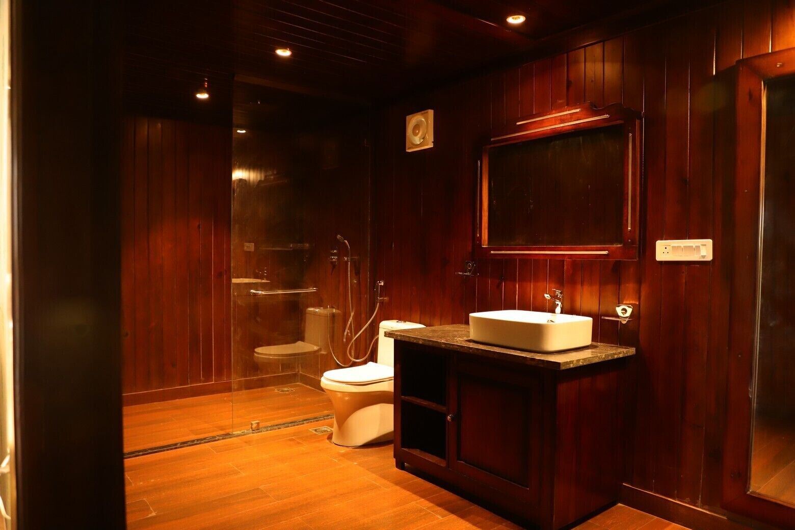 A wooden-paneled bathroom with a toilet, shower, and sink.